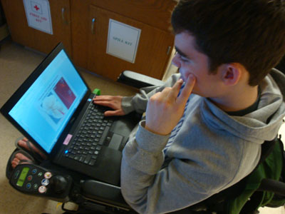 A student sitting in a wheelchair uses a laptop